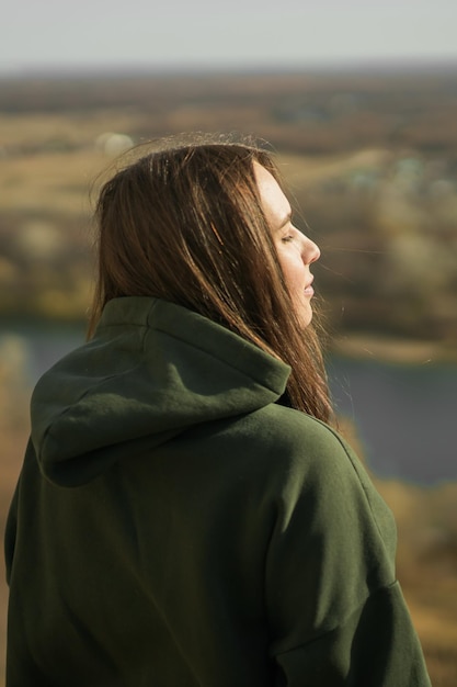 Rear view of trendy young woman in dark green hoodie in autumn cute model walks in park in golden au