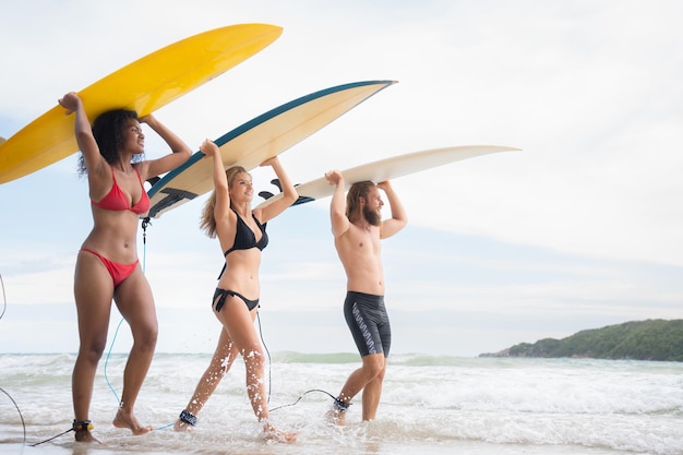 サーフボードを頭に乗せ、サーフィンするために海に入っていく2人の女性と若い男性の背面図