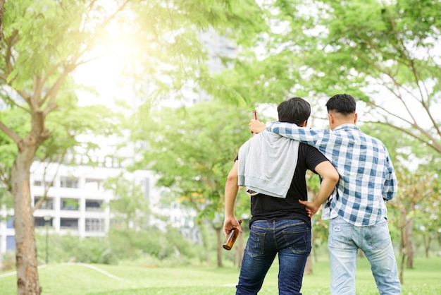 ビールを持って立って屋外で話している2人の若い友人の背面図