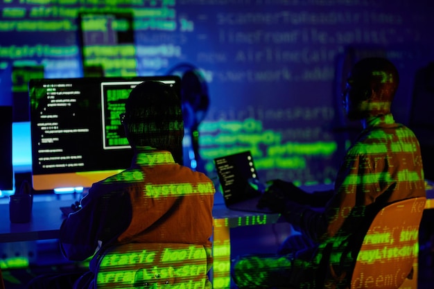 Rear view of two young programmers sitting in front of computers by desks