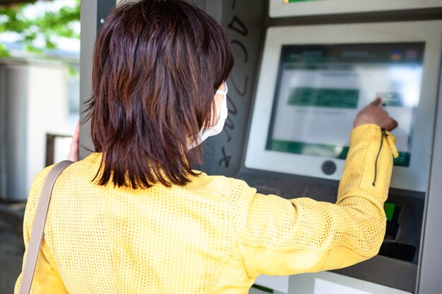 Rear view of an unidentified woman in a protective mask points her finger at blurry information board