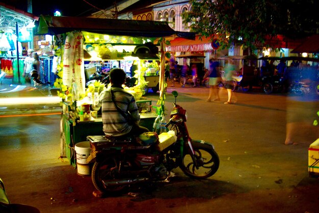 rear view of vendor sitting on motorcycle in illuminated city at night