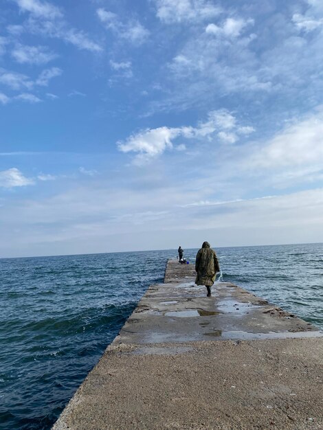 바다 해변에서 콘크리트 부두를 걷는 어부의 후면보기 수직 샷