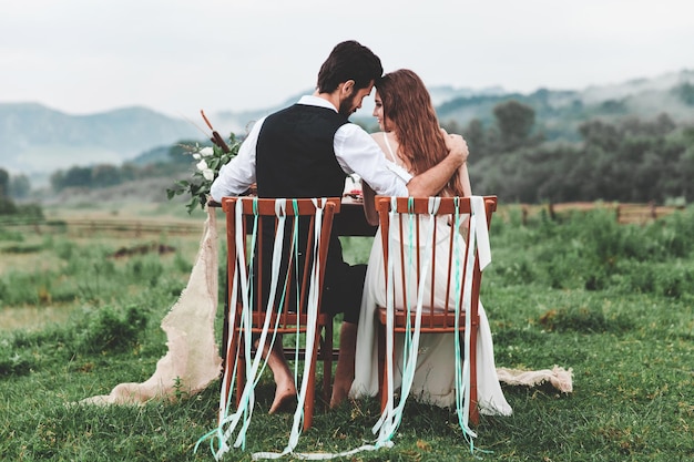 Photo rear view of wedding couple sitting on chairs at farm