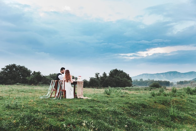 Photo rear view of wedding couple sitting on chairs at farm