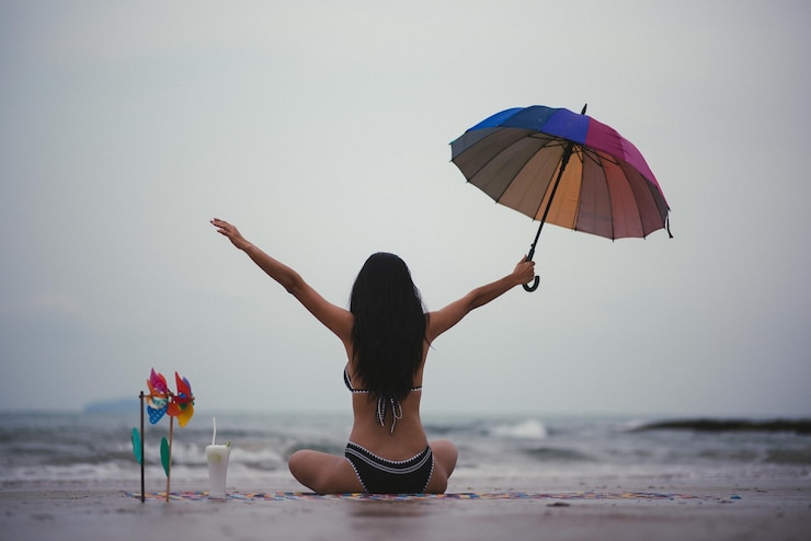 फोटो rear view of woman in bikini with arms outstretched sitting at beach against sky