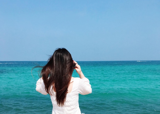 Rear view of woman by sea against clear sky