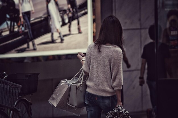Foto vista posteriore di una donna che porta delle borse mentre cammina per strada