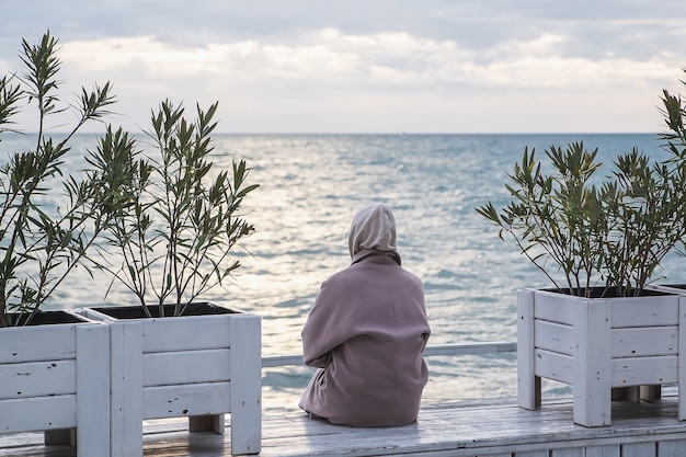 Vista posteriore di una donna in cappotto che guarda al mare nella stagione fredda.