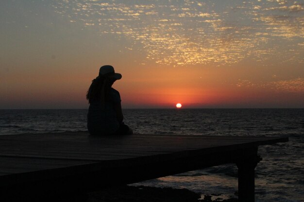 Vista posteriore di una donna che contempla il tramonto in riva al mare