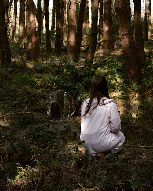 Foto vista posteriore di una donna accovacciata contro gli alberi nella foresta