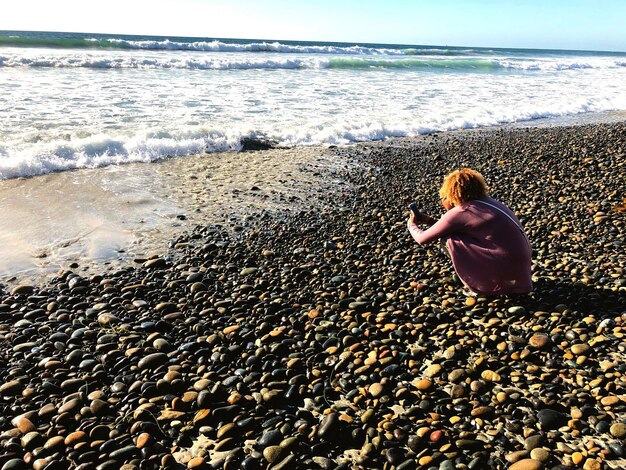 Photo rear view of woman crouching on beach against sky