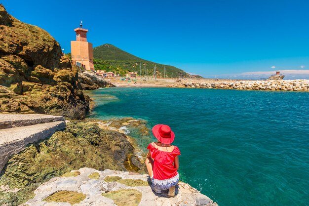 Foto vista posteriore di una donna accovacciata su formazioni rocciose sul mare contro il cielo blu