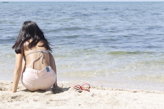 Rear view of woman crouching on shore at beach