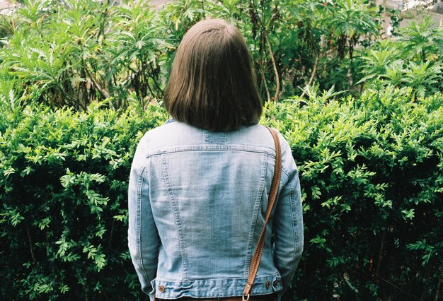 デニムジャケットを着た女性が緑の植物に立っている後ろの景色