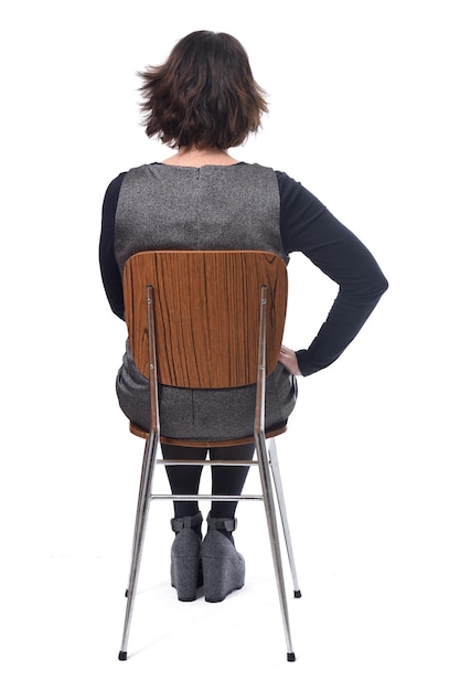 Rear view of woman in dress sitting on a white background, hand on hip