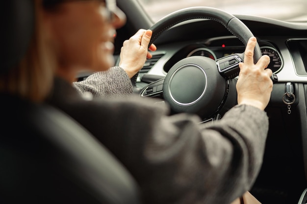 Вид сзади женщины за рулем автомобиля и держащей обе руки на руле по дороге на работу