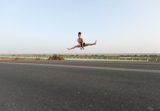 Rear view of woman exercising on road against clear sky