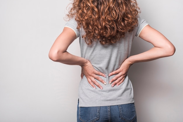 rear view of woman having backache against gray background