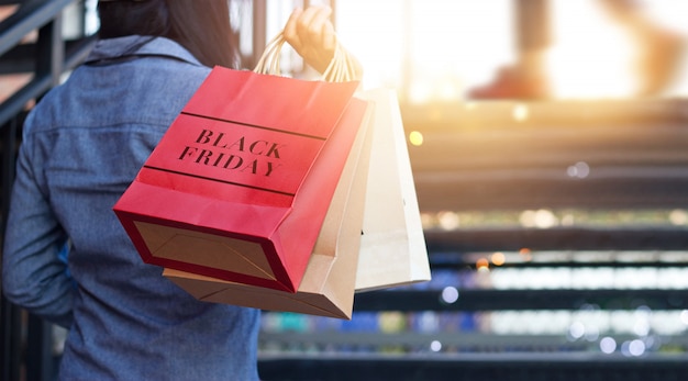 Retrovisione della donna che tiene il sacchetto della spesa di black friday mentre sulle scale all'aperto sul centro commerciale