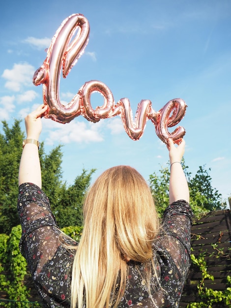 Photo rear view of woman holding love text against sky