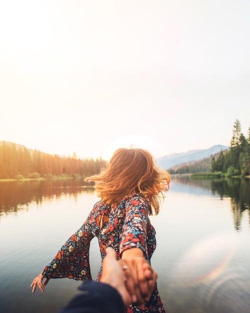 Rear view of woman holding man hand by lake against clear sky