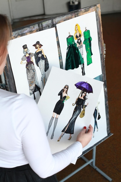 Photo rear view of woman holding papers with designs by easel