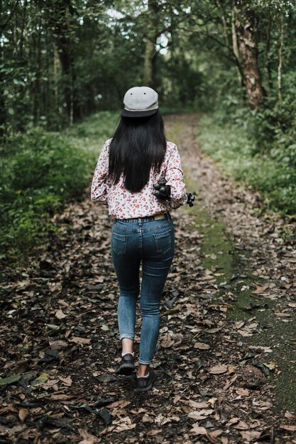 Rear view of woman holding tripod while walking on footpath in forest