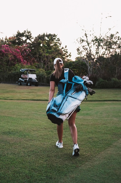 Rear view of a woman is walking with a bag on her shoulder containing golf clubs