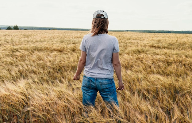 Вид сзади женщина в джинсах среди желтых сухих злаков пшеничное поле сельское хозяйство и урожай зерна макет дружелюбный