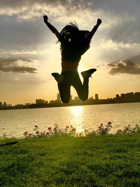 Photo rear view of woman jumping against lake during sunset