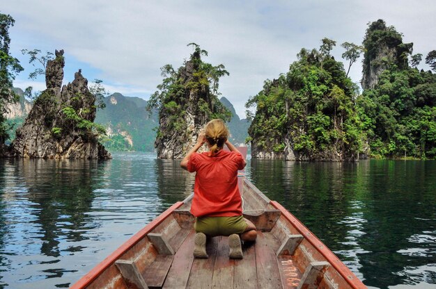Foto vista posteriore di una donna inginocchiata su una barca mentre guarda le formazioni rocciose del lago