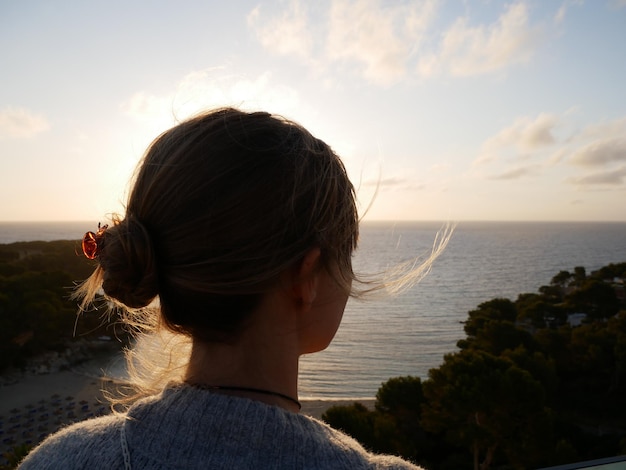 Foto vista posteriore di una donna che guarda il mare contro il cielo durante il tramonto.