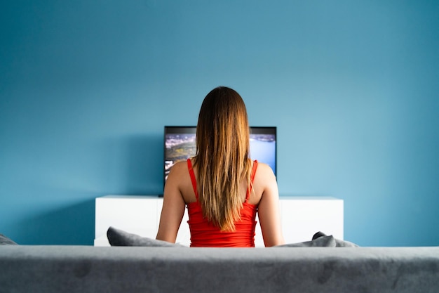 Photo rear view of woman looking at television set against blue wall at home