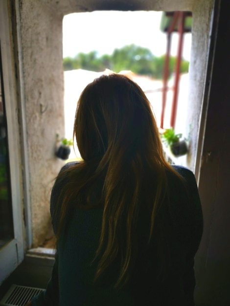 Photo rear view of woman looking through window