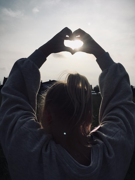 Foto vista posteriore di una donna che fa la forma di un cuore contro il cielo