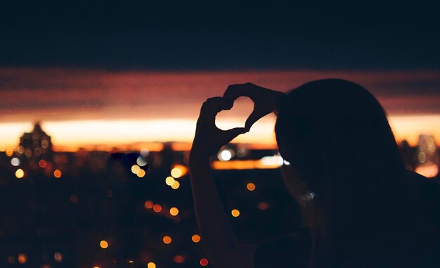 Photo rear view of woman making heart shape at night