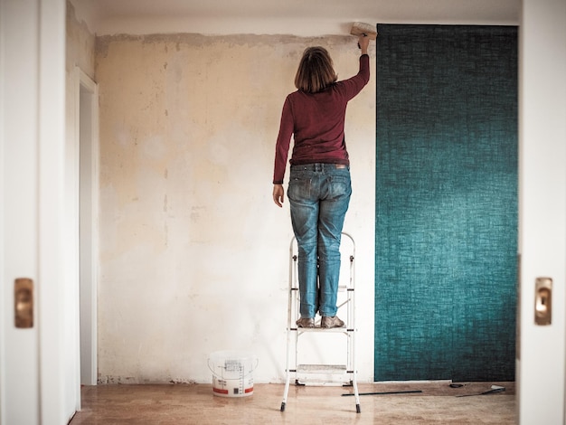 Rear view of woman painting wall while standing on step ladder at home