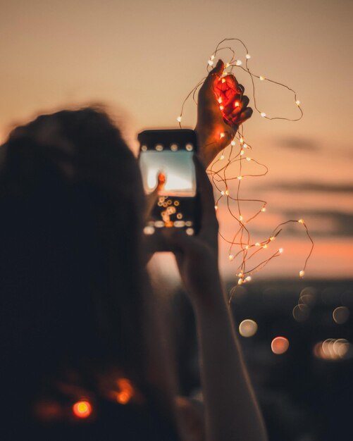 Photo rear view of woman photographing while holding illuminated string lights