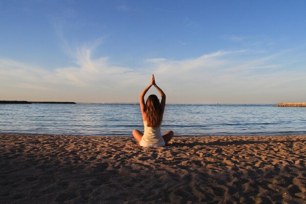 Foto vista posteriore di una donna che pratica yoga sulla spiaggia contro il cielo al mattino