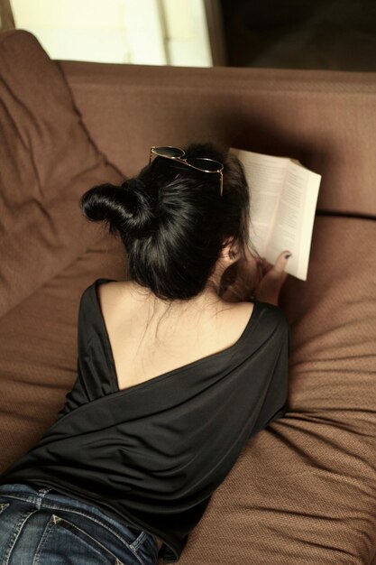 Photo rear view of woman reading book on sofa at home