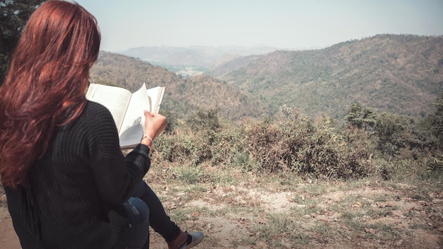 Foto vista posteriore di una donna che legge un libro mentre è seduta contro la montagna