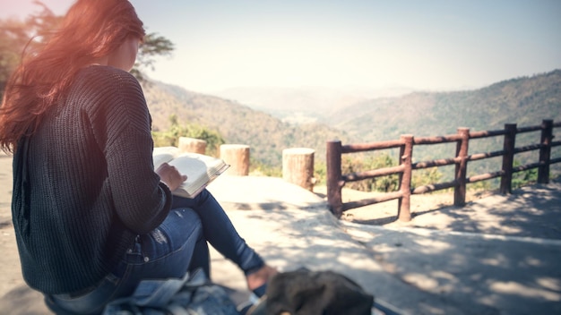 Rear view of woman reading book while sitting against mountain