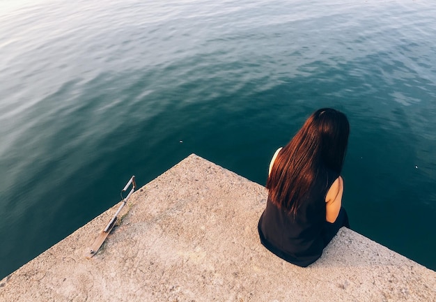 Foto vista posteriore di una donna che si rilassa su un muro di sostegno vicino al mare