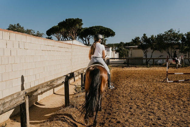 Rear view of a woman rider warming up with her horse around the equestrian arena