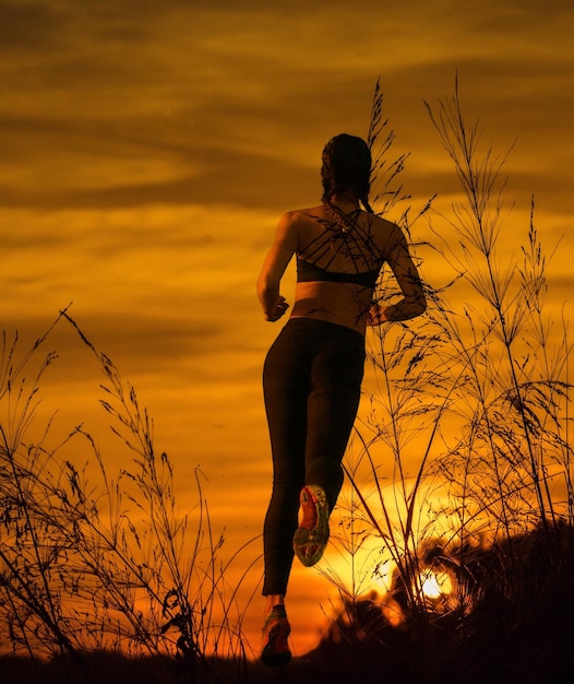 Foto vista posteriore di una donna che corre sul campo contro un cielo arancione