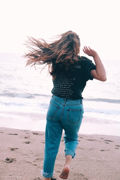 Photo rear view of woman running on sand towards sea at beach