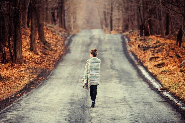 Photo rear view of woman in shawl walking on road in forest