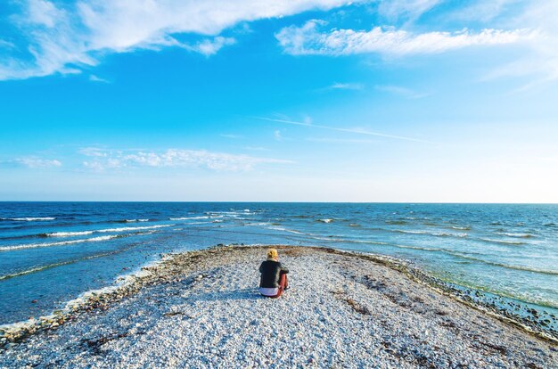 Rear view of woman sitting at beach against blue sky