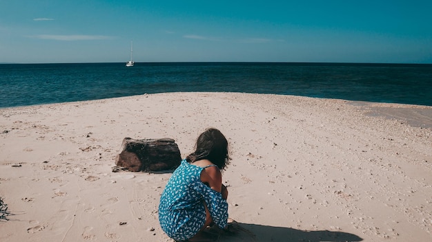 Foto vista posteriore di una donna seduta sulla spiaggia contro il mare